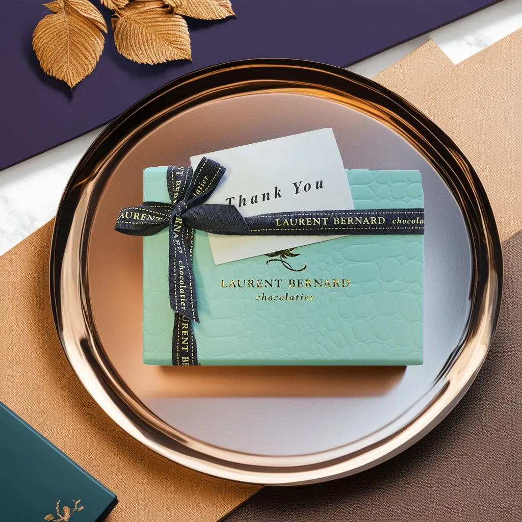 Mint Laurent Bernard chocolate box tied with a black ribbon and a "Thank You" card on a gold tray